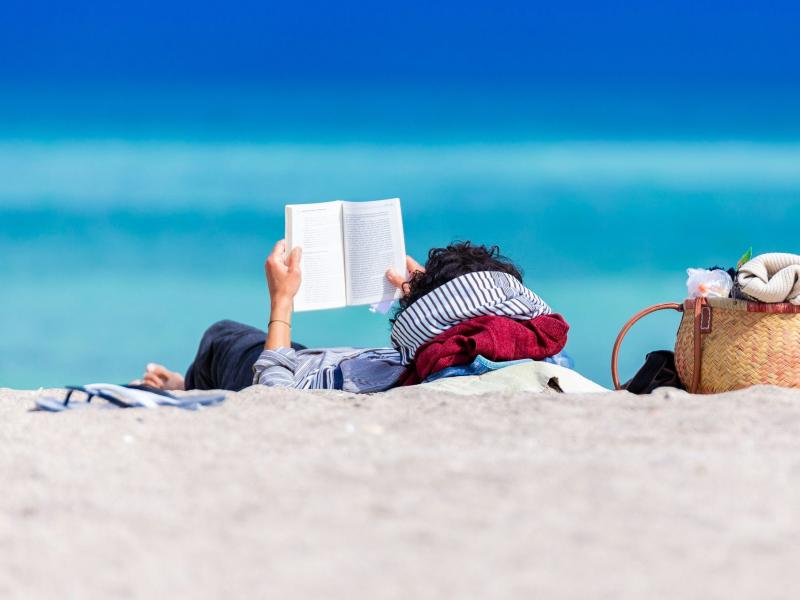 Kvinde ligger på stranden og læser.