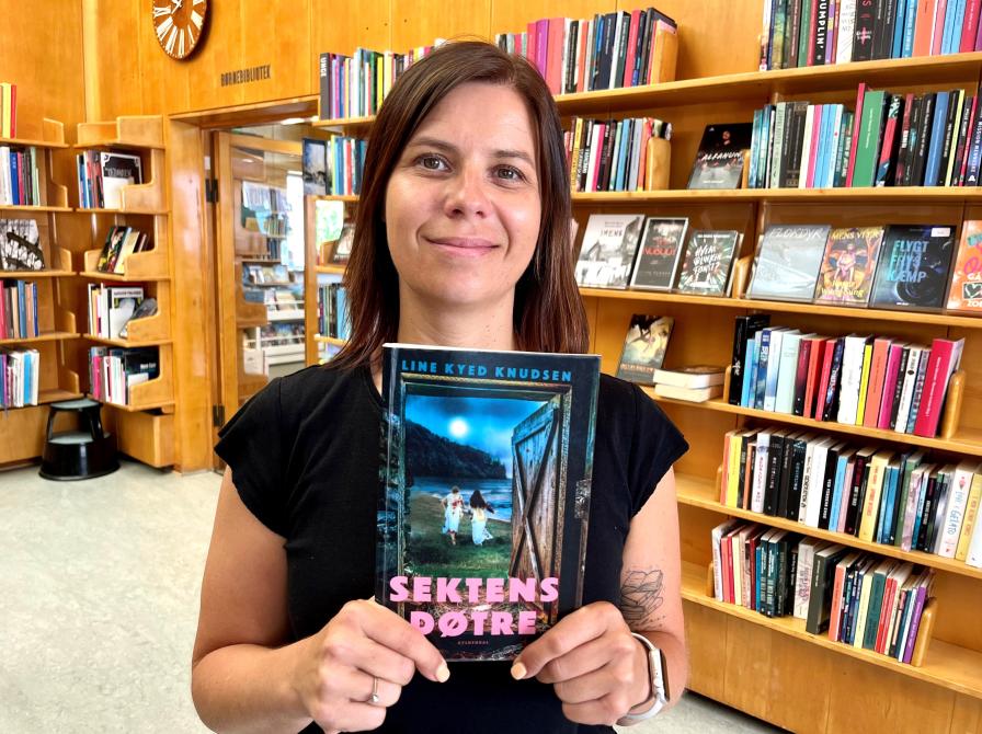 Bibliotekar Marianne Wismar Mühring står med bogen "Sektens døtre".